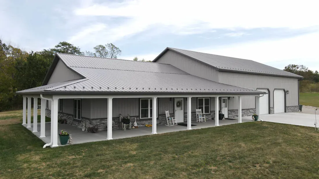Grey steel post-frame home with standing seam roof, stone wainscot and wrap-around white-post porch