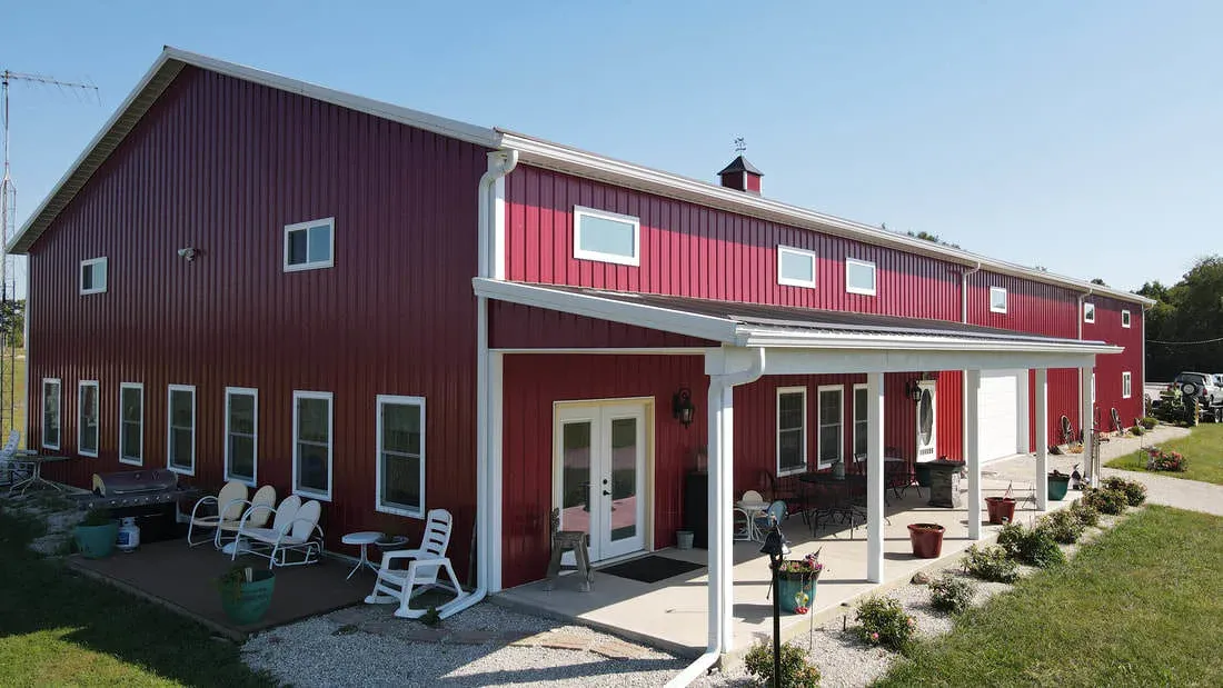 Deep red two-story steel building with white trim, covered patio and cupola