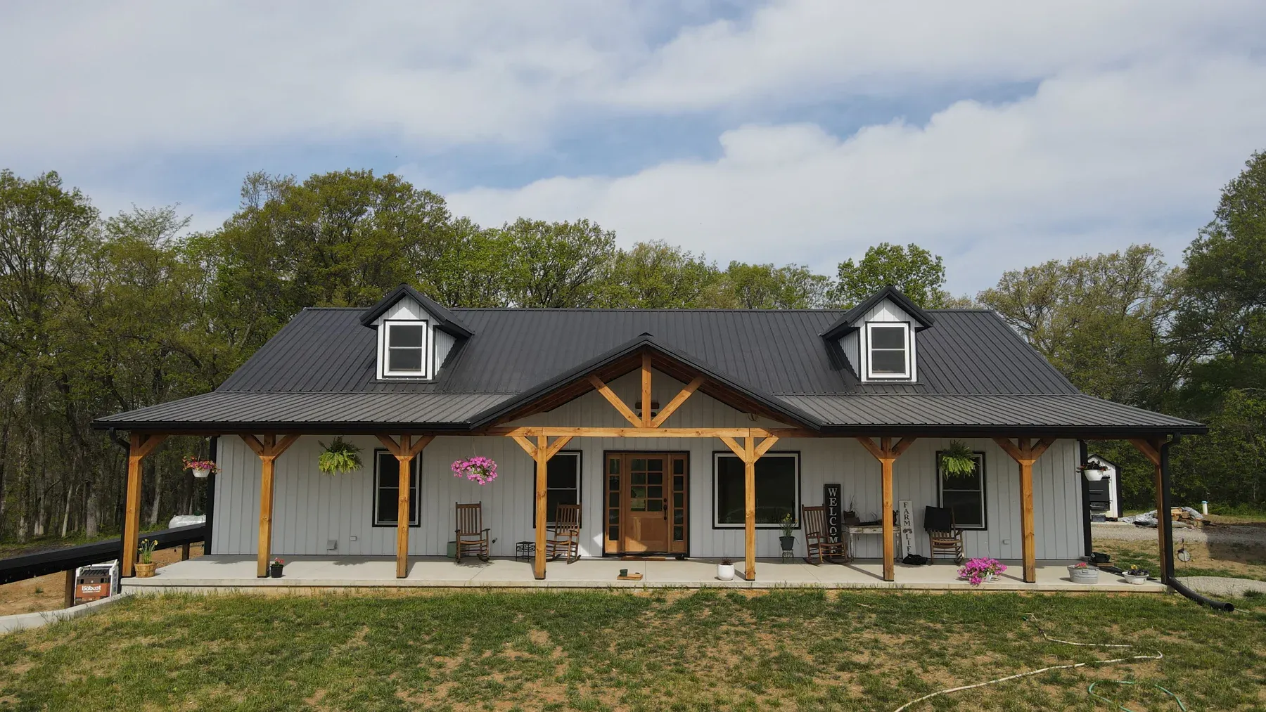 Light grey steel home with black metal roof, dormers and timber truss covered porch