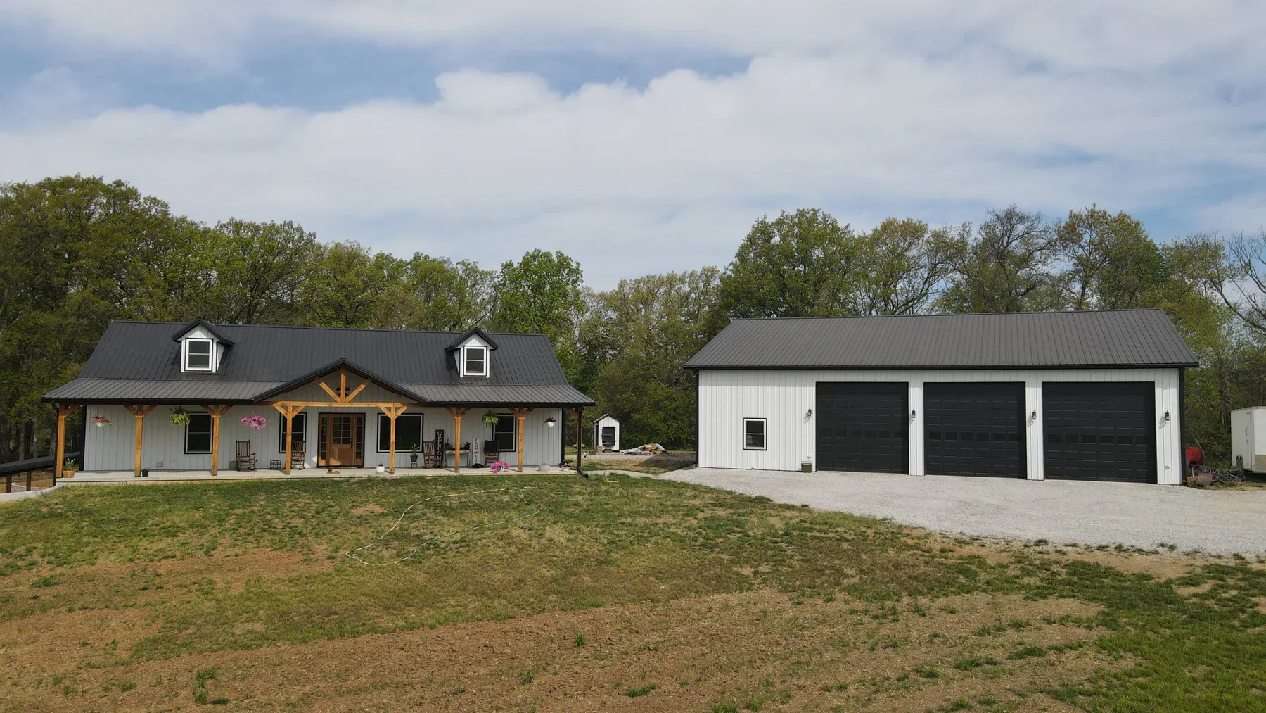 White steel home with black metal roof beside a matching three-bay garage with black doors