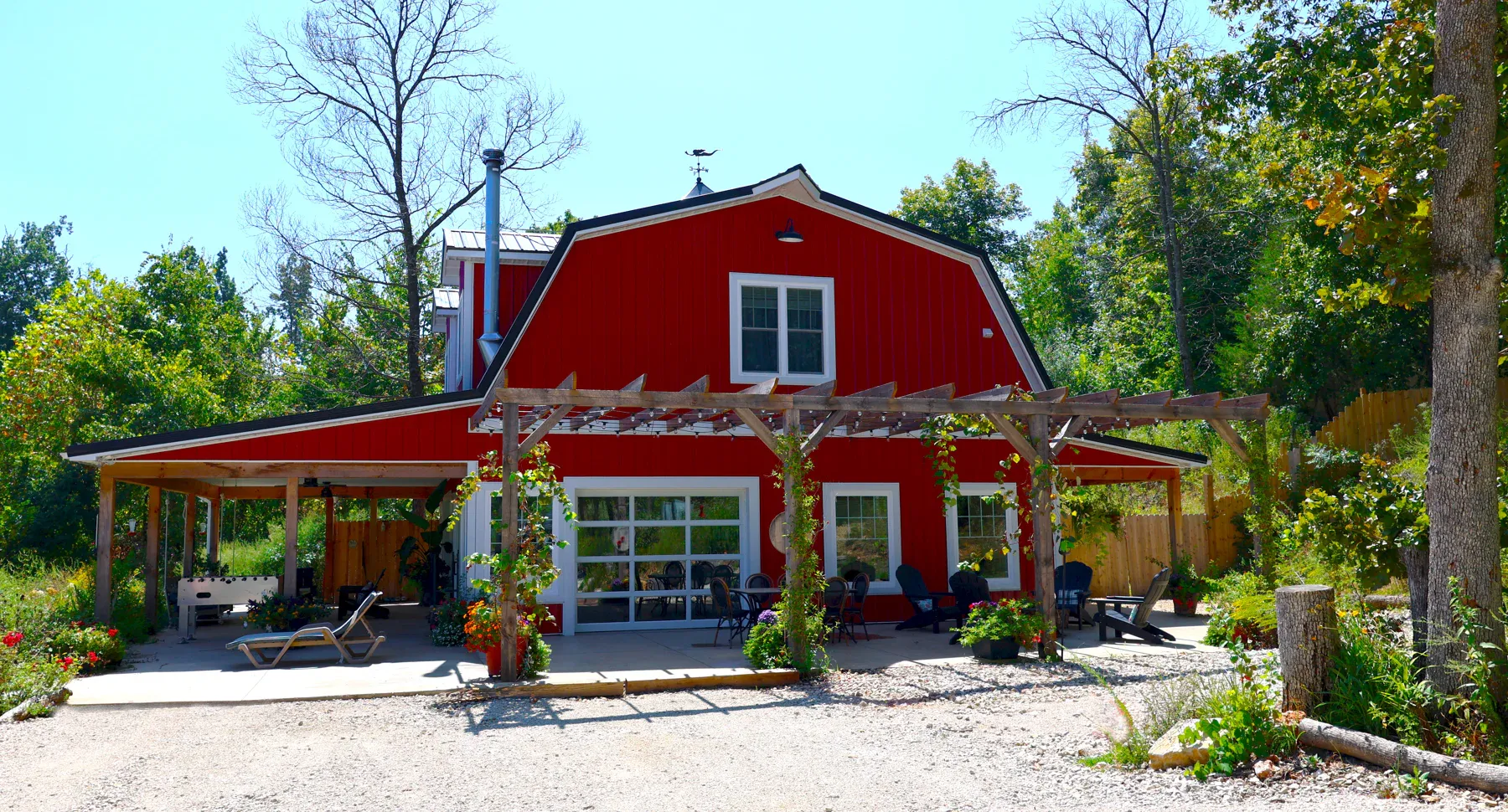 Red gambrel steel barn with white trim, pergola patio and glass overhead door
