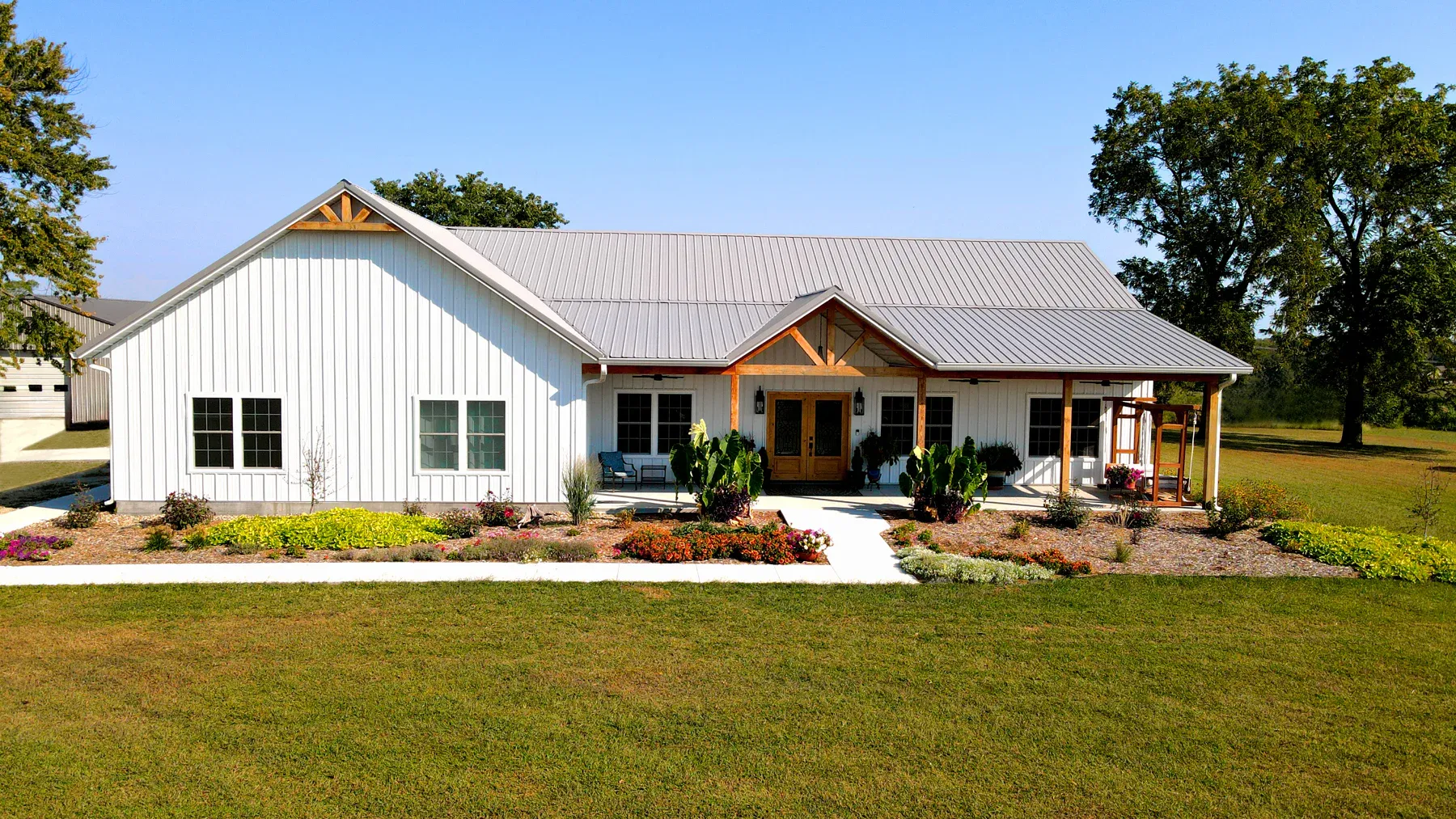 White steel ranch home with silver metal roof, timber truss gable and covered side porch