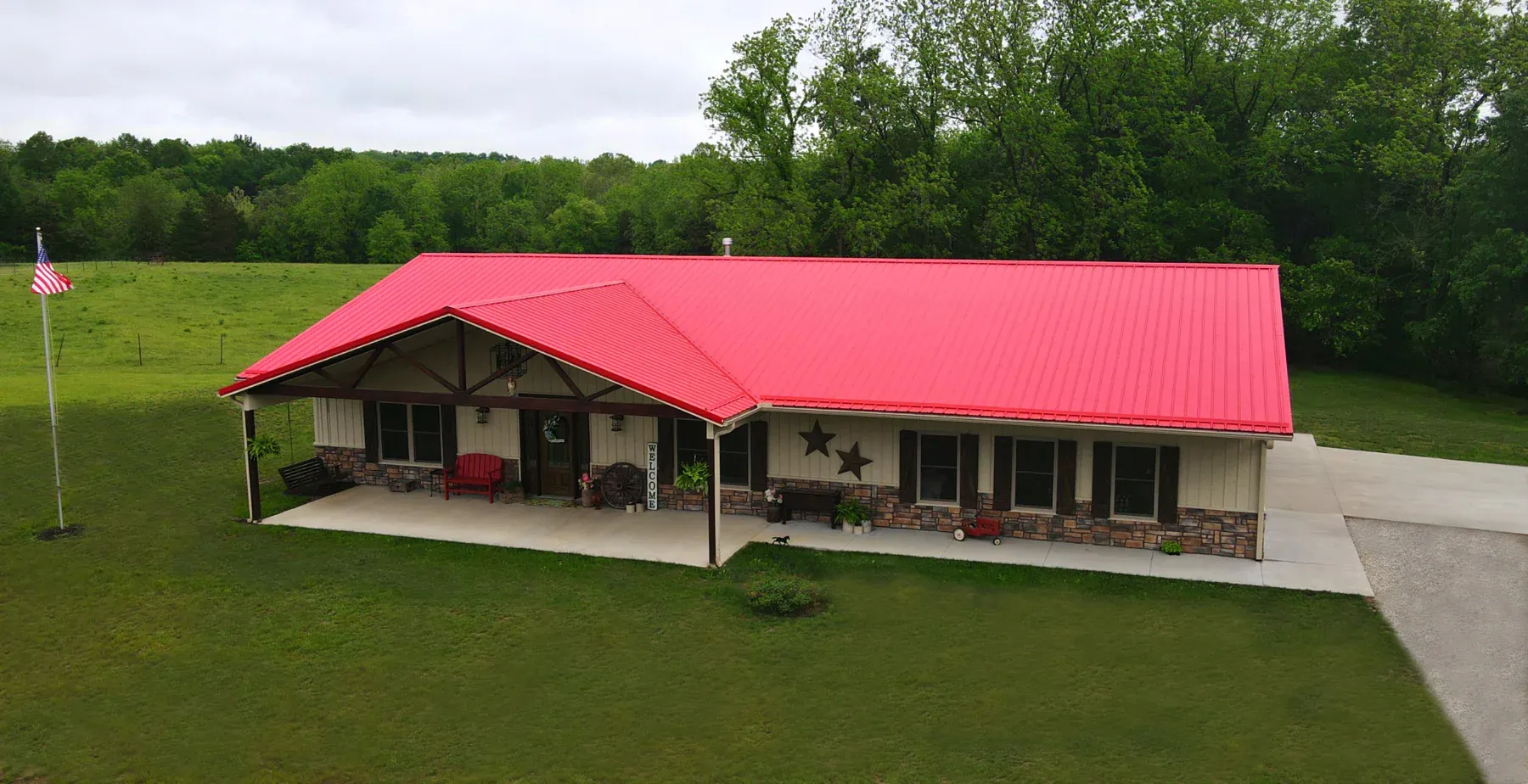 Cream steel ranch home with bright red metal roof, timber truss porch and stone wainscot