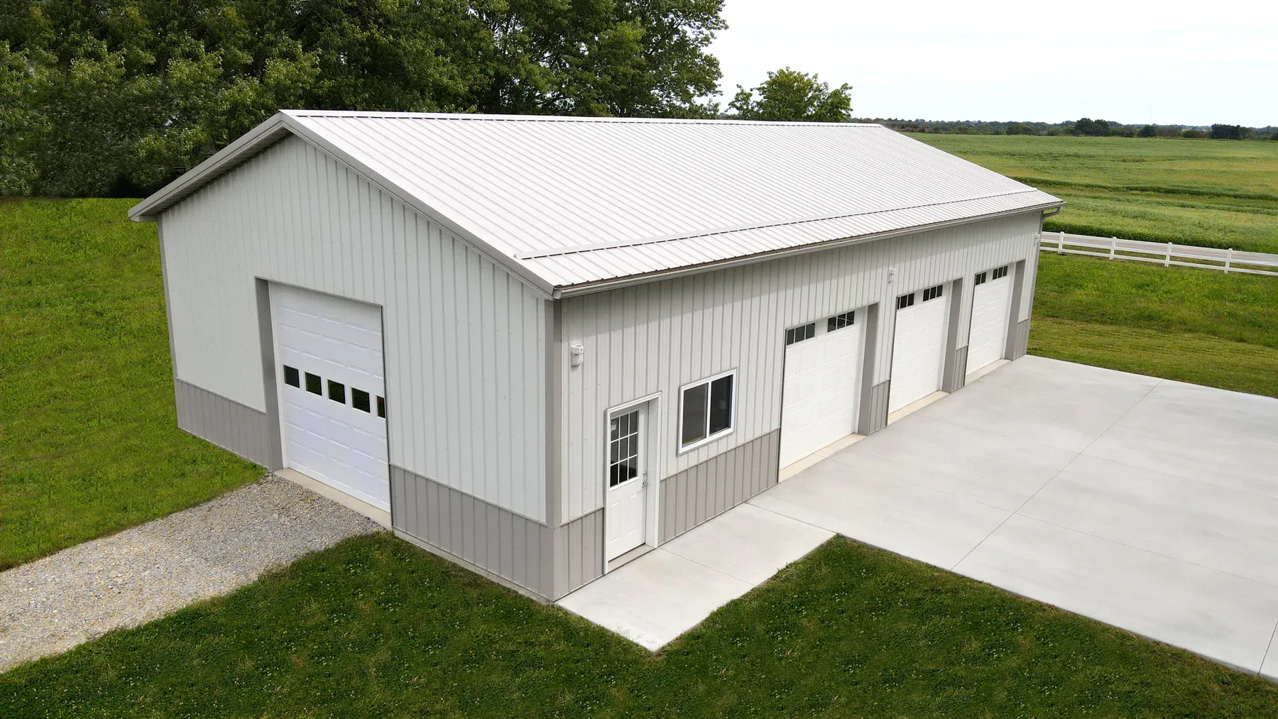 White steel garage with grey wainscot, silver roof and four white overhead doors