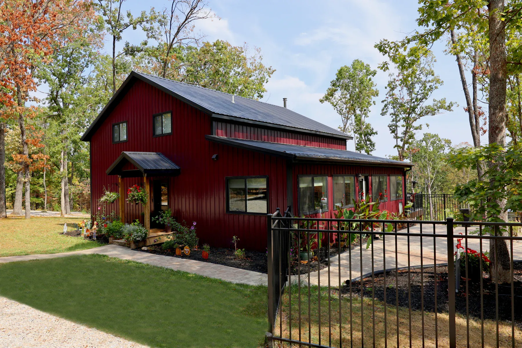 Deep red two-story steel home with black metal roof, gable entry canopy and wide windows