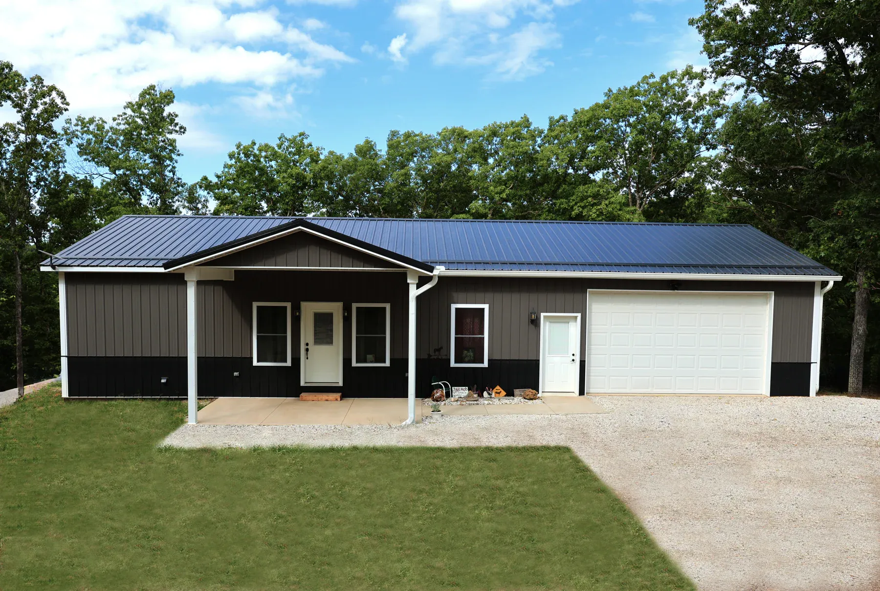 Brown steel home with black wainscot, navy metal roof, covered porch and attached garage