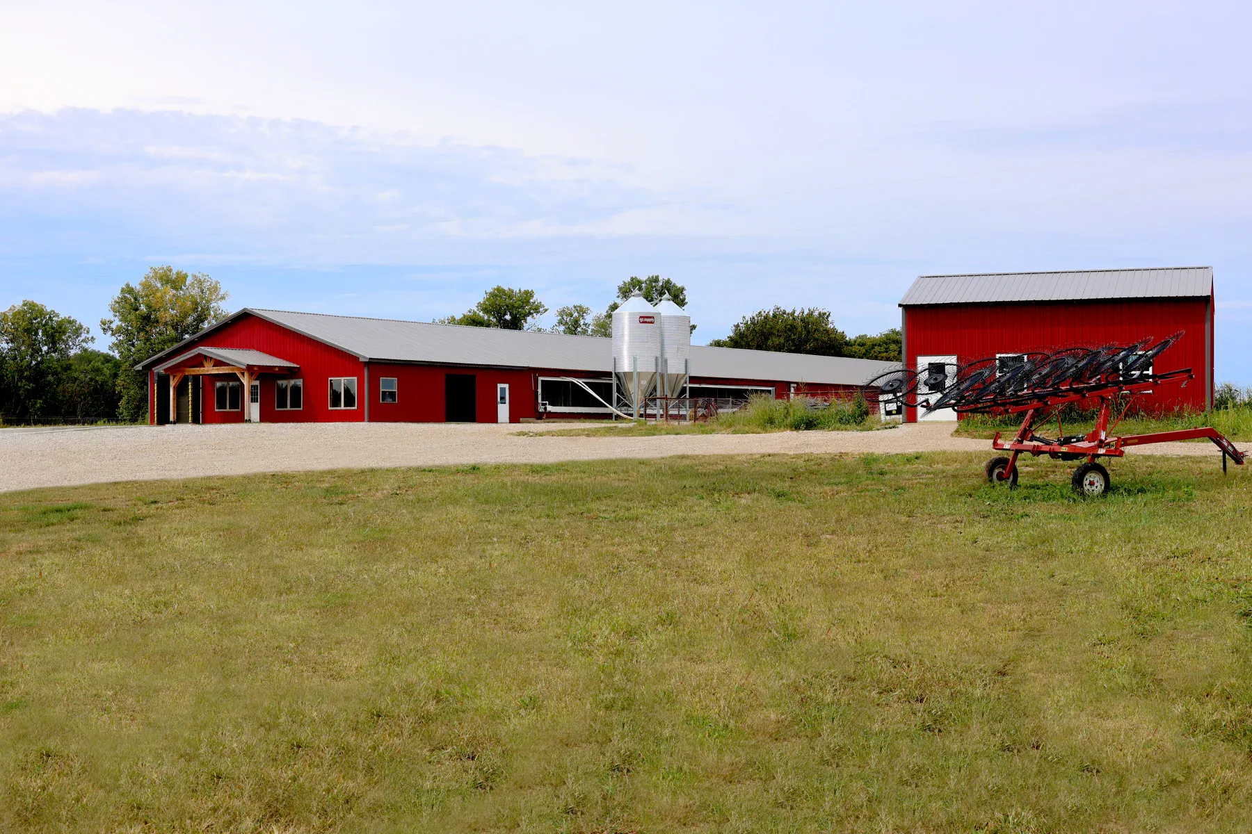 Red steel farm complex with long equipment building, grain bins and matching red barn