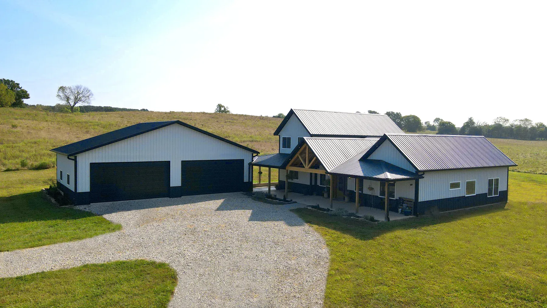 White steel home with black wainscot and timber porch beside a matching two-bay garage