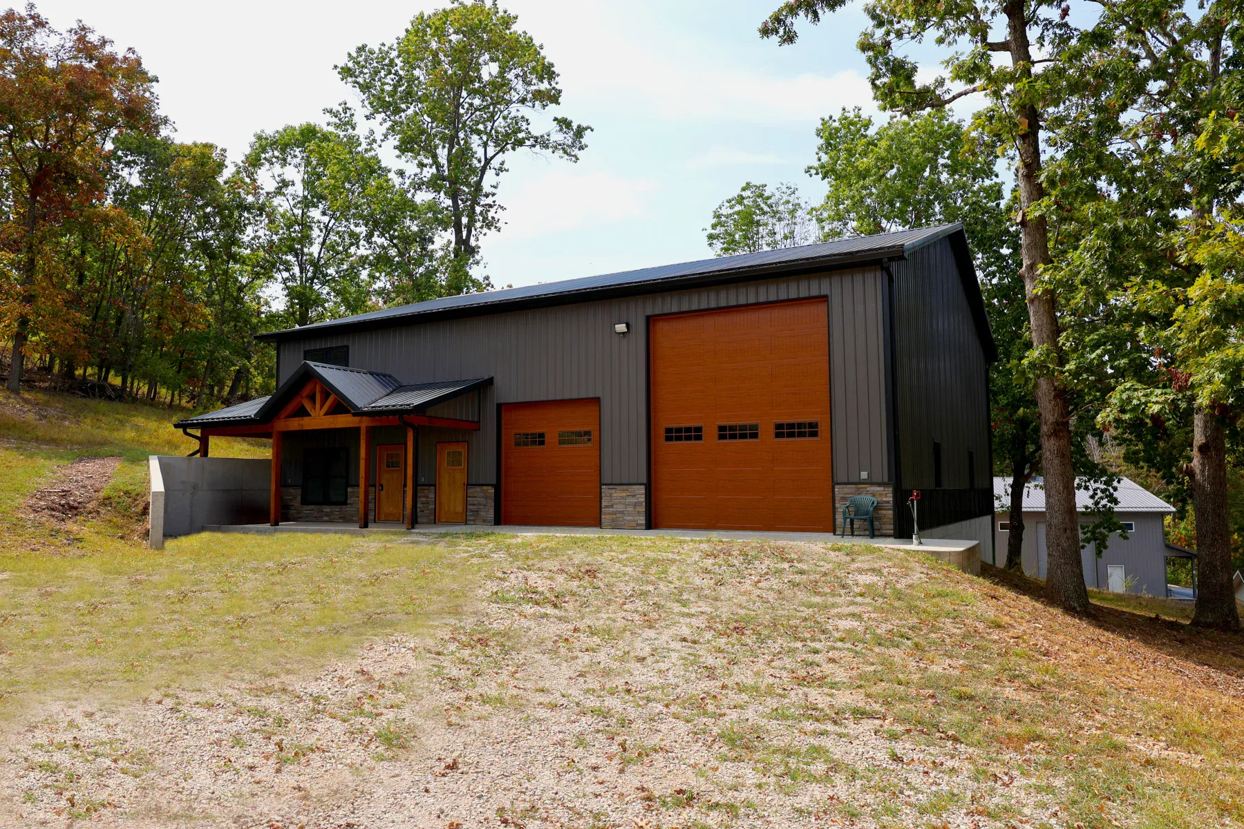 Charcoal steel shop with black metal roof, wood-look overhead doors and timber truss entry