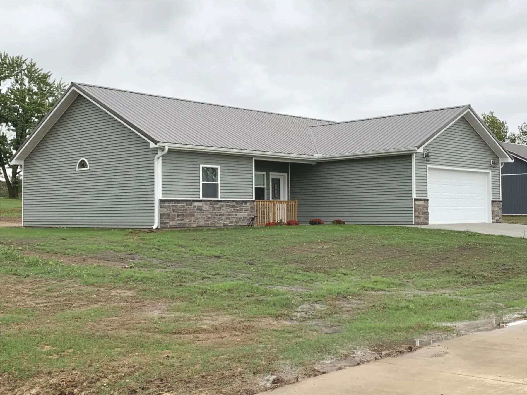 Grey ranch home with brown standing seam metal roof, stone wainscot and two-car garage
