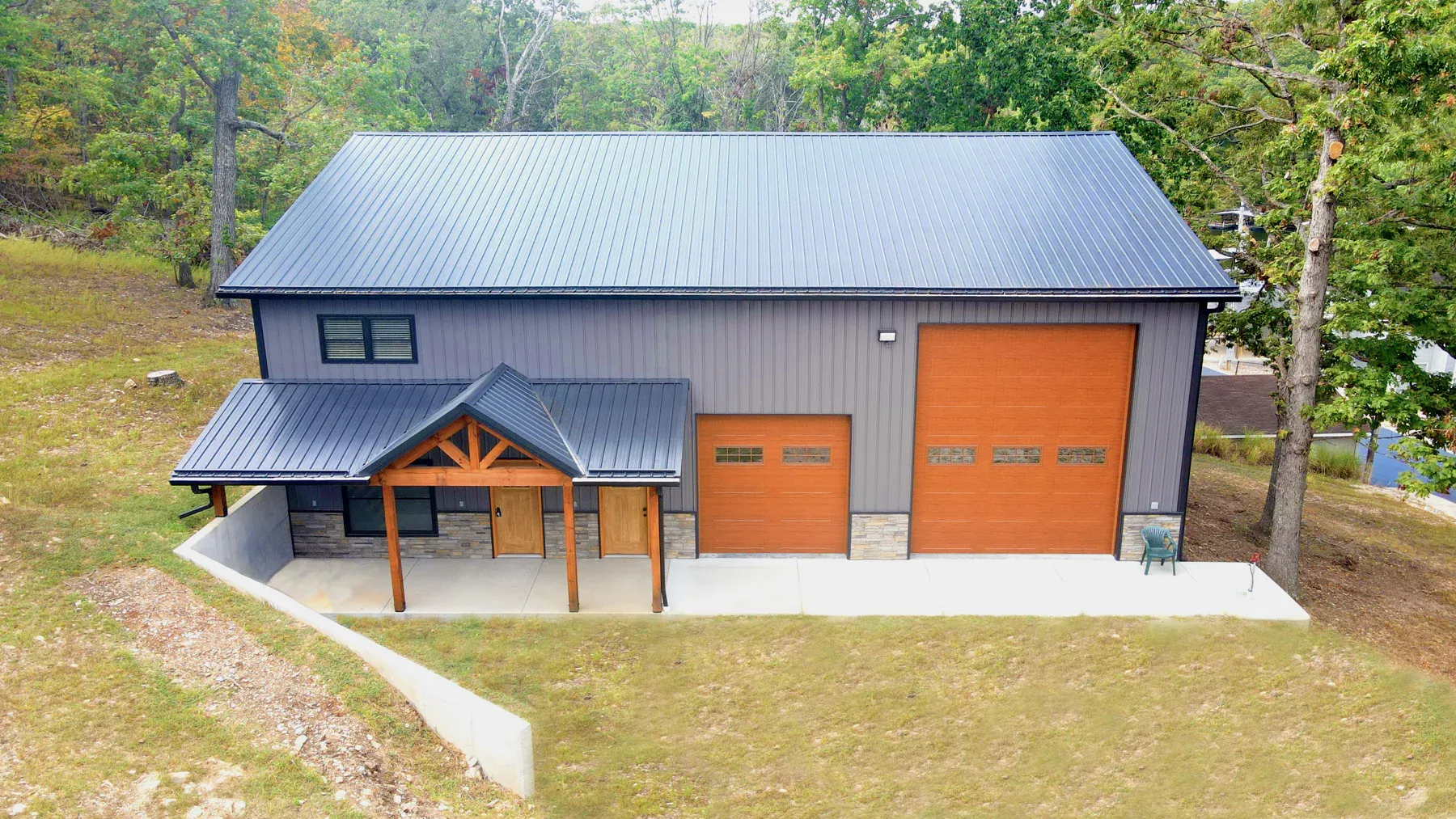 Grey steel shop with dark metal roof, wood-look overhead doors and stone timber porch
