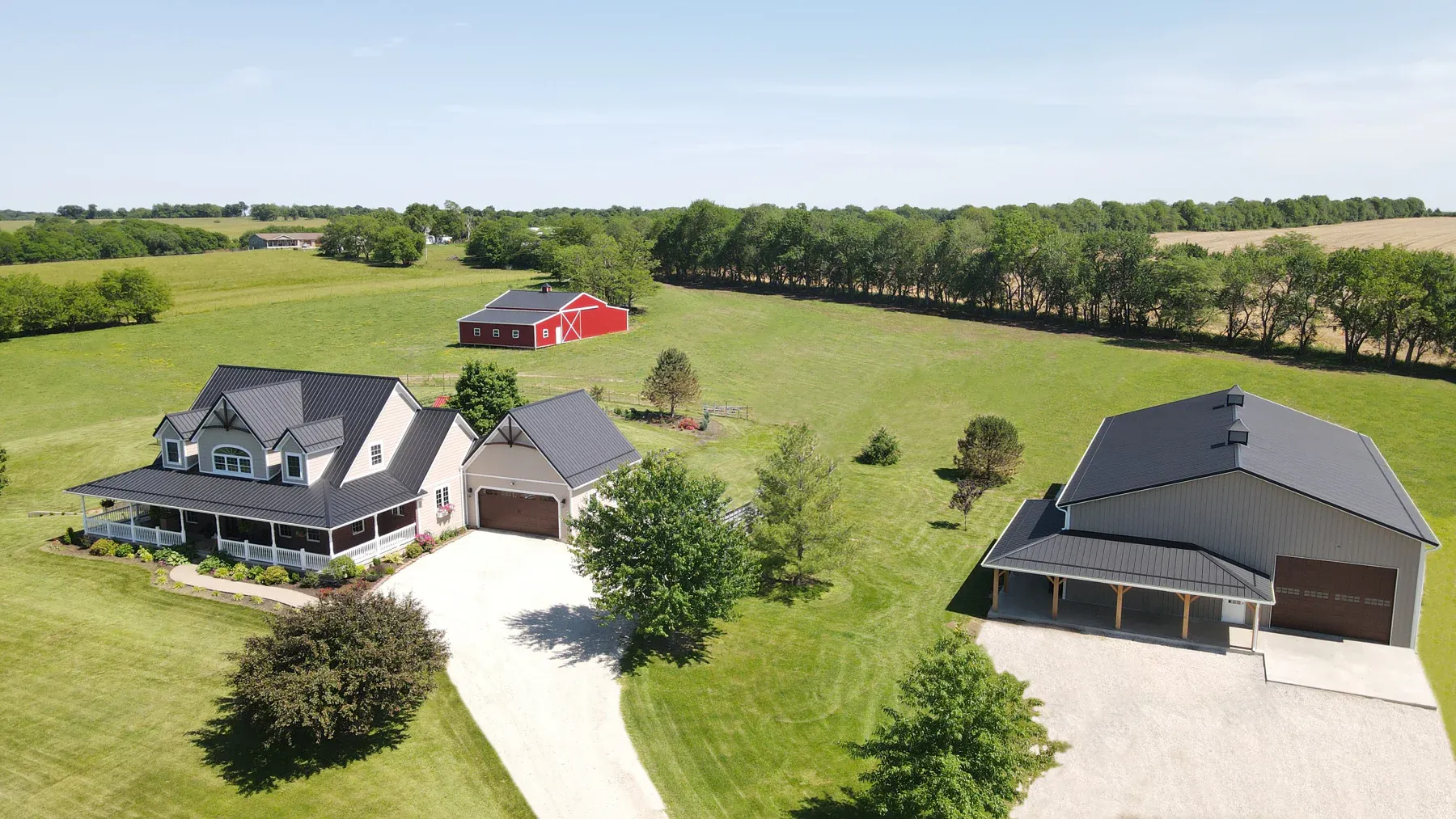 Aerial view of a farmstead with metal-roof home, tan pole barn and red barn on acreage