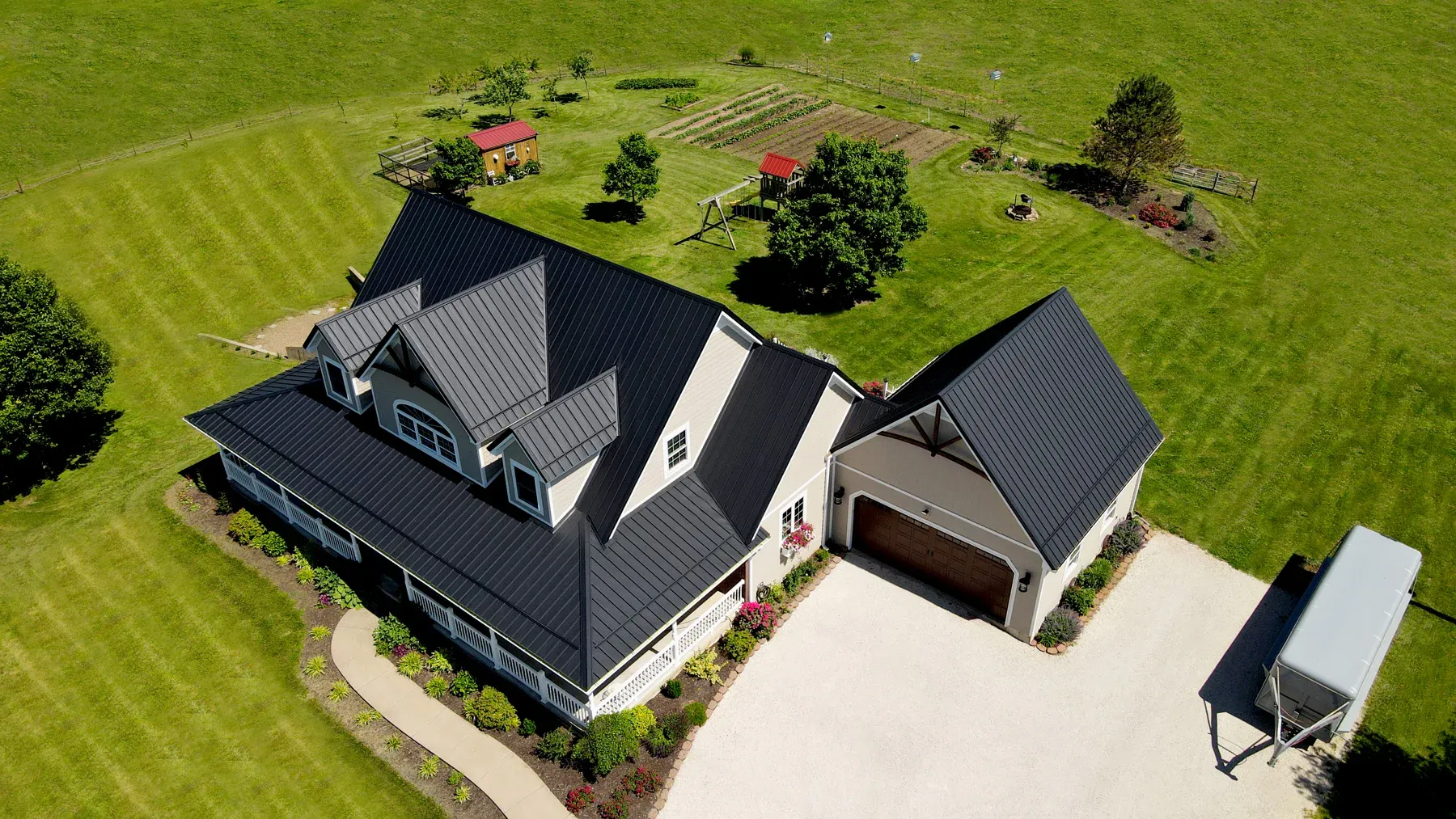 Aerial view of a tan home with black standing seam metal roof, dormers and attached garage