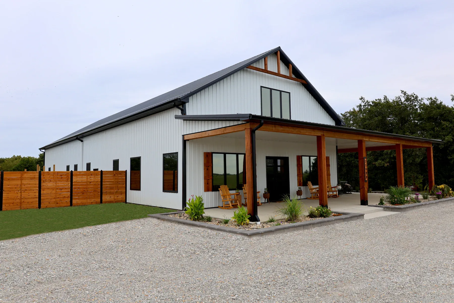 White steel barndominium with black roof, cedar posts and long covered patio