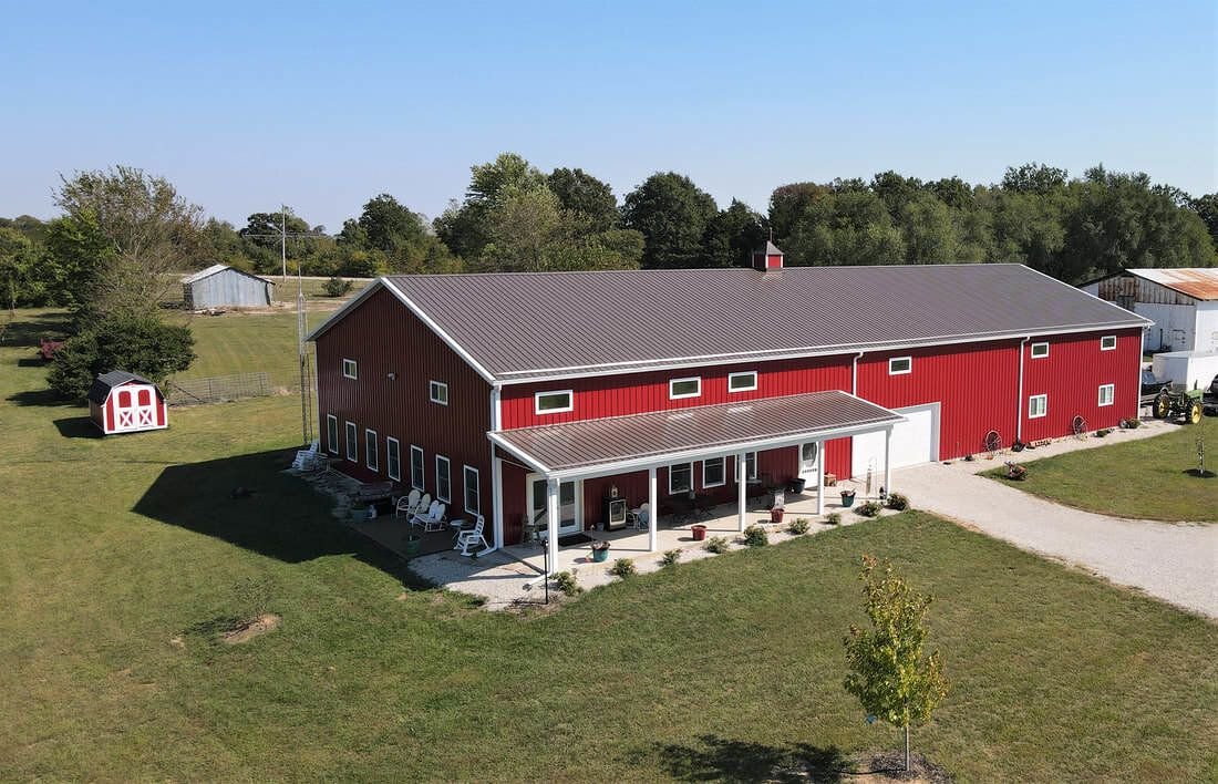 Aerial view of a large red steel barndominium with brown metal roof and covered porch