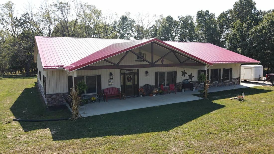 Cream steel home with red metal roof, timber truss entry and long covered porch