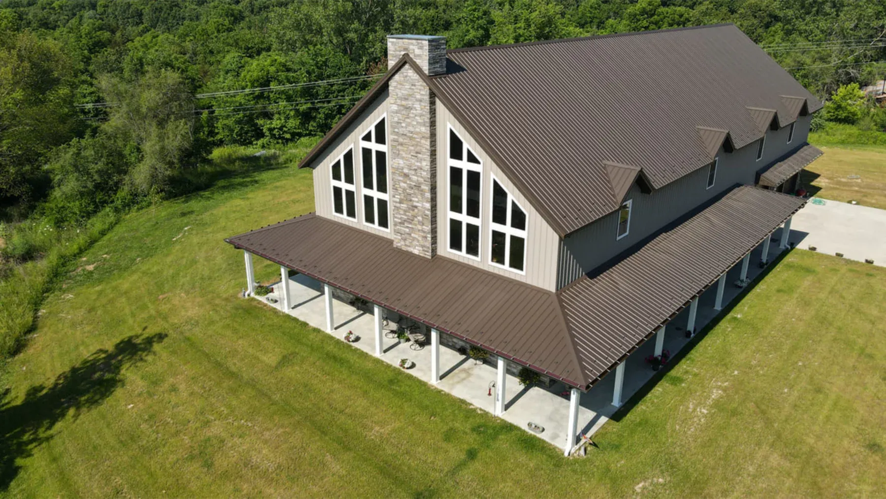 Aerial view of a tan steel lodge with brown metal roof, stone chimney and tall prow windows